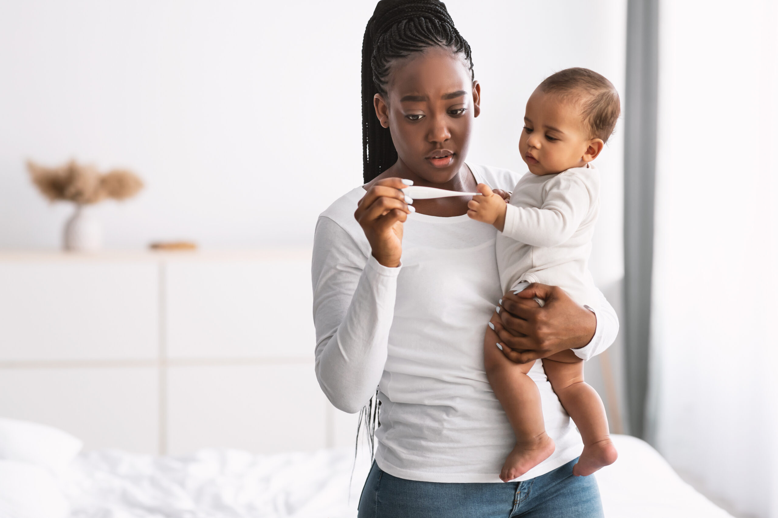 Children Healthcare. Portrait of scared young African American mother looking at thermometer and holding her adorable small black baby on hands at home. Sick infant kid having fever