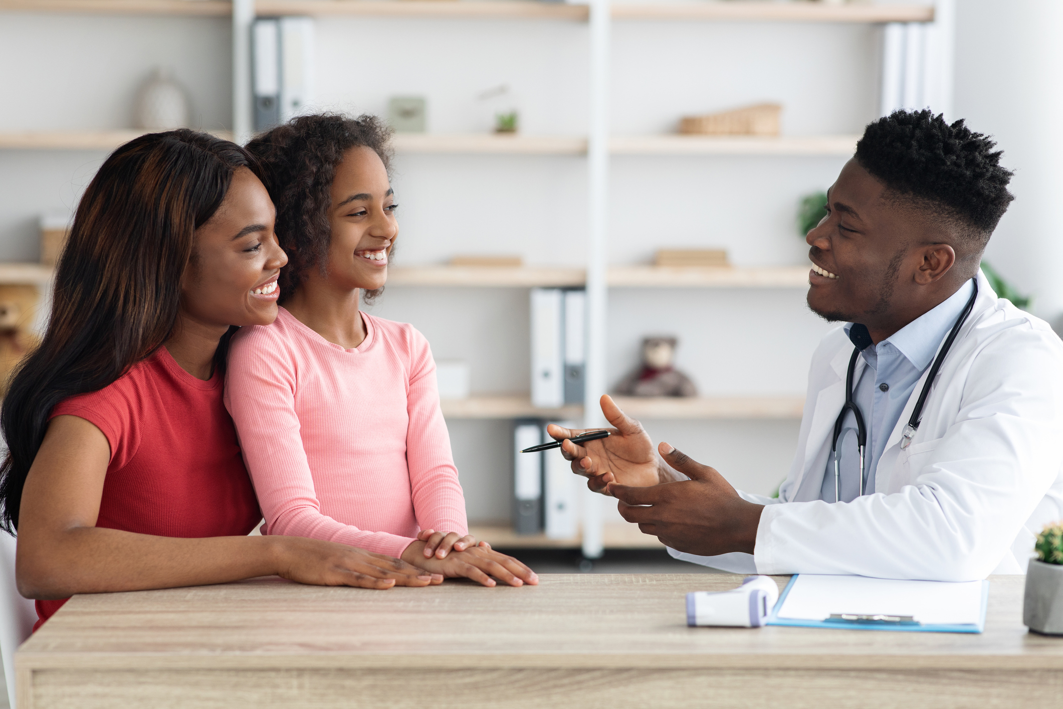 Cheerful african american mother and daughter teenager having appointment with pediatrician handsome black man at modern clinic, side view, copy space. Healthcare for children concept